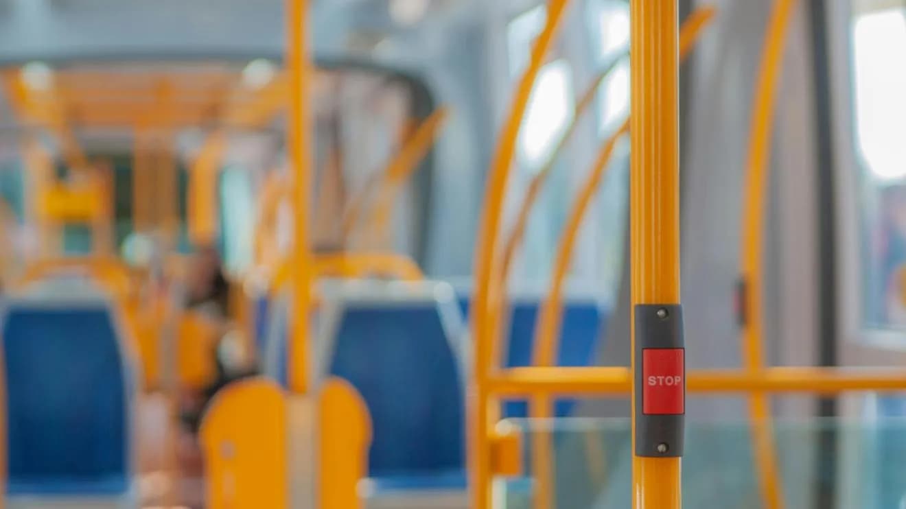 A red stop button on a yellow pole inside a bus, with blurry blue seats in the background.